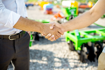 Buyer shaking hand with salesman on the open ground of the agricultural shop, having a deal,...