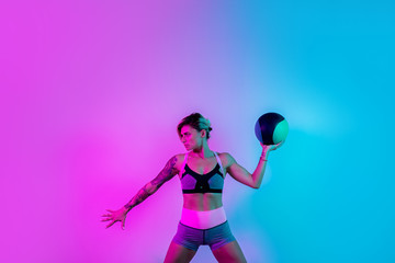 Fit young blonde woman exercise with medicine ball in gym in neon lights.