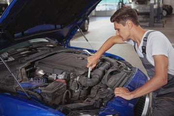 Male auto mechanic repairing broken automobile at his workshop. Professional auto technician working at the garage