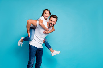 Portrait of cheerful people laughing piggyback wearing white t-shirt denim jeans isolated over blue background - obrazy, fototapety, plakaty