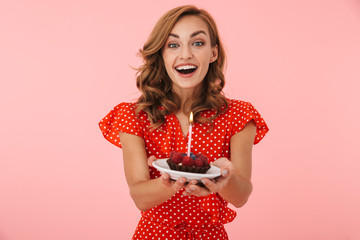 Cheery positive happy young woman posing isolated over pink wall background holding birthday cake.