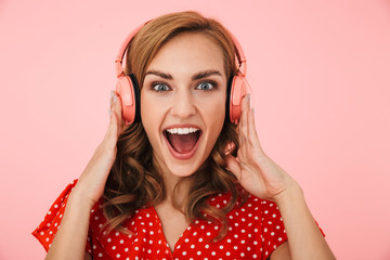 Pleased emotional happy young woman posing isolated over pink wall background listening music with...