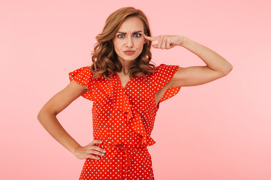 Displeased young woman posing isolated over pink wall background showing finger crazy gesture near head.