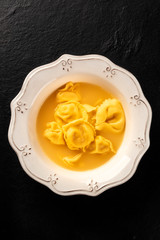 Italian tortellini with broth, shot from above on a black background with a place for text