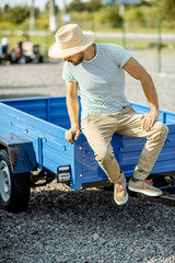 Portrait of a young agronomist sitting on the farm truck trailer at the open ground of agricultural shop