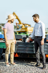 Agronomist with salesman choosing a new farm truck trailer, standing on the open ground of the agricultural shop