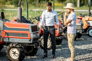 Young agronomist with elegant salesman choosing a tractor for farming on the open ground of agricultural shop