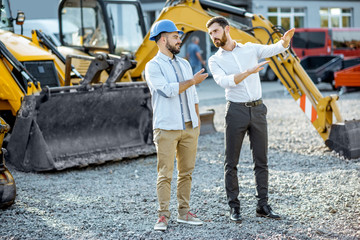 Builder choosing heavy machinery for construction with a sales consultant on the open ground of a shop with special vehicles