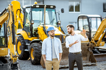 Builder choosing heavy machinery for construction with a sales consultant on the open ground of a shop with special vehicles