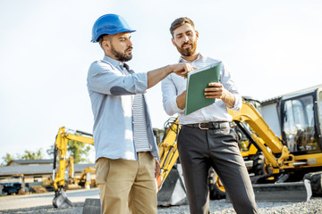 Builder choosing heavy machinery for construction with a sales consultant standing with some...