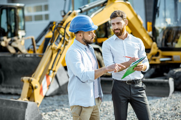 Builder choosing heavy machinery for construction with a sales consultant standing with some...