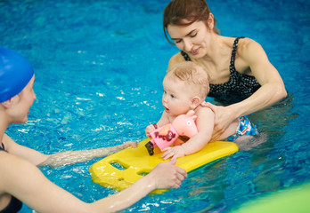 Swimming instructor teaching and helping little baby floating in blue water using auxiliary swimming tools for protection. Family healthy active lifestyle, early development, happy childhood concept