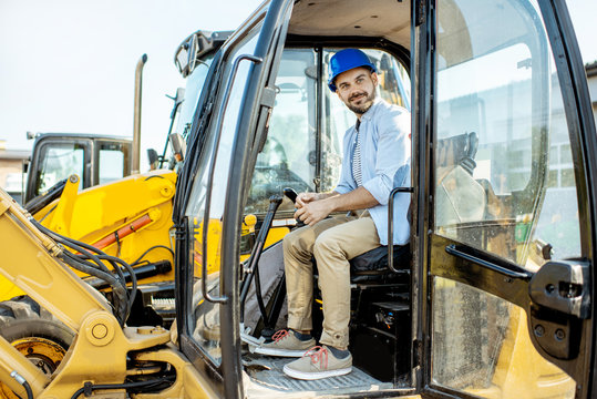 Handsome builder trying escavator while buying a new heavy machinery for construction on the open ground of the shop