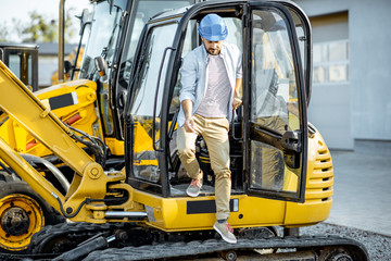 Handsome builder or construction worker getting out of the escavator on the construction site
