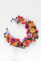 A mix of fruits, berries and blooms arranged in a wreath on a white background with a copy space