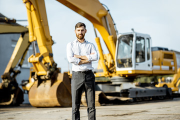 Portrait of a handsome sales consultant or manager standing on the open ground of the shop with heavy machinery for construction
