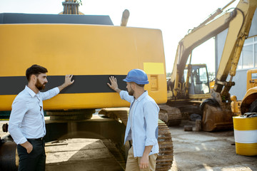 Builder choosing heavy machinery for construction, talking with a sales consultant on the open...
