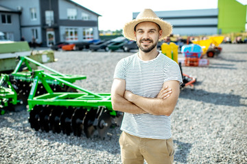Portrait of a young agronomist standing near the plow at the outdoor ground of the shop, buying new...