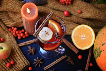 Autumn mulled wine based on red wine with orange, apple and spicy cinnamon sticks, and star anise on a black background. Traditional autumn drink on a background of leaves.