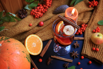 Autumn mulled wine based on red wine with orange, apple and spicy cinnamon sticks, and star anise on a black background. Traditional autumn drink on a background of leaves.