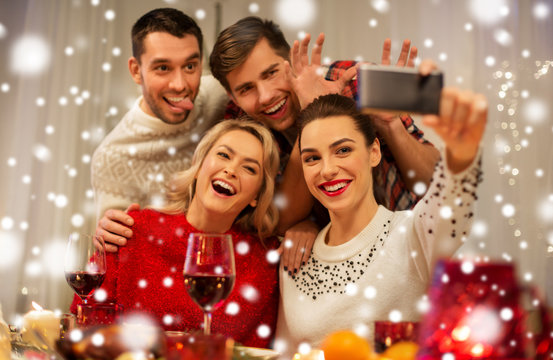 holidays and celebration concept - happy friends taking selfie by smartphone at home christmas dinner over snow
