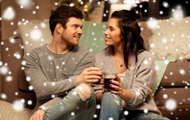 christmas, leisure and people concept - happy couple drinking coffee and eating at home over snow
