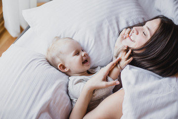 Happy mother and baby playing in bed. Happy family concept.