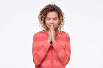 Gorgeous young asian woman with dreadlocks holding hands in namaste or prayer, keeping eyes closed...