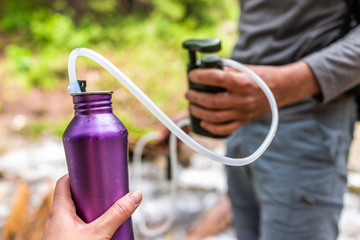 Man and woman couple using water filter on hiking trail river in Colorado to purify drinking water...