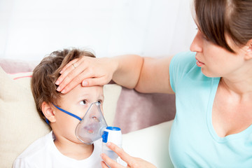 Young woman doing inhalation with a nebulizer son and touches his forehead