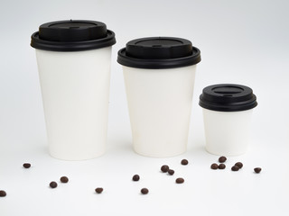 From small to big a line of white paper cups with coffee beans isolated on white. Coffee shop mockup with copyspace