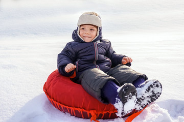 Fototapeta na wymiar happy joyful beautiful child boy rides from the mountain on a red tubing in winter