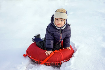 happy joyful beautiful child boy rides from the mountain on a red tubing in winter