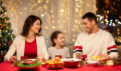 holidays, family and celebration concept - happy mother, father and little daughter having christmas dinner at home