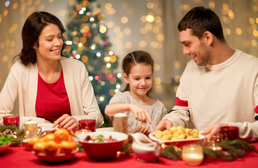 holidays, family and celebration concept - happy mother, father and little daughter having christmas dinner at home