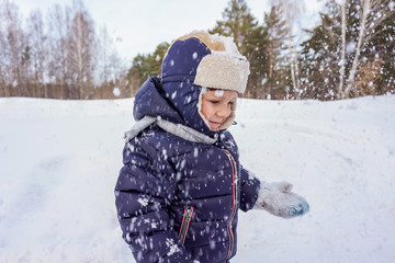 portrait of a happy child boy throws snow, snowflakes in the air in cold winter against the background of snowdrifts