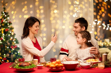 holidays, family and celebration concept - happy mother, father and little daughter having christmas dinner and taking picture by smartphone at home