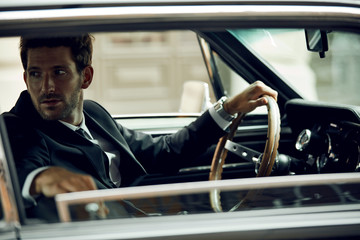 Handsome man in black suit driving a classic car