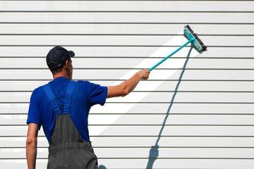 White man in overalls washes the wall with a brush.
