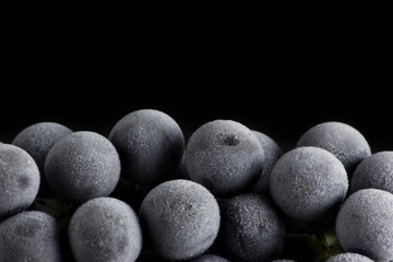 a frozen and frosted bunch of grapes lies on the mirror surface of the table against a black background.