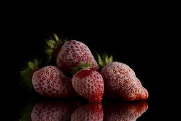 four red frozen strawberries covered with hoarfrost lie on a mirror surface on a black background.