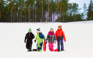 childhood, sledging and season concept - group of happy little kids with sleds in winter over forest background