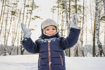 portrait of a happy child boy throws snow, snowflakes in the air in cold winter against the background of snowdrifts