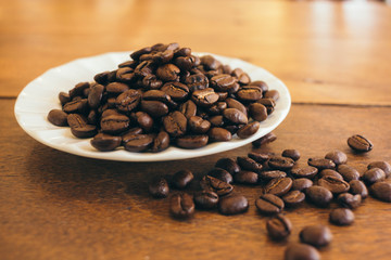Coffee beans in a white plate on a wooden table