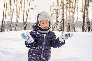 portrait of a happy child boy throws snow, snowflakes in the air in cold winter against the background of snowdrifts