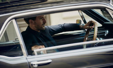 Handsome man in black suit driving a classic car