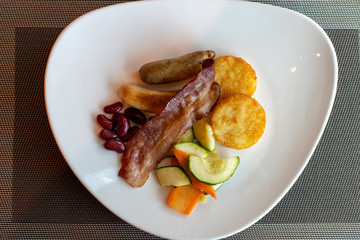 What is served for breakfast at the hotel. Classic breakfast. Potato pancakes with sausages and bacon, as well as some beans.