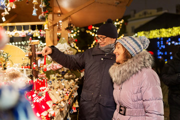 shopping, winter holidays and people concept - happy senior couple at christmas market souvenir shop stall on town hall square in tallinn, estonia