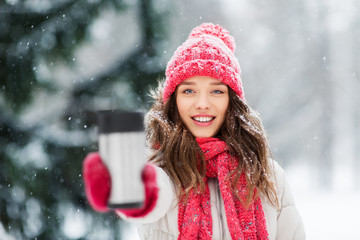 people, season, drinks and christmas concept - happy teenage girl or young woman with hot drink in tumbler outdoors in winter park