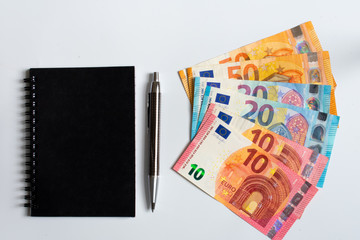 Black notes, pen and fifty twenty and ten euro banknotes isolated on white background top view 